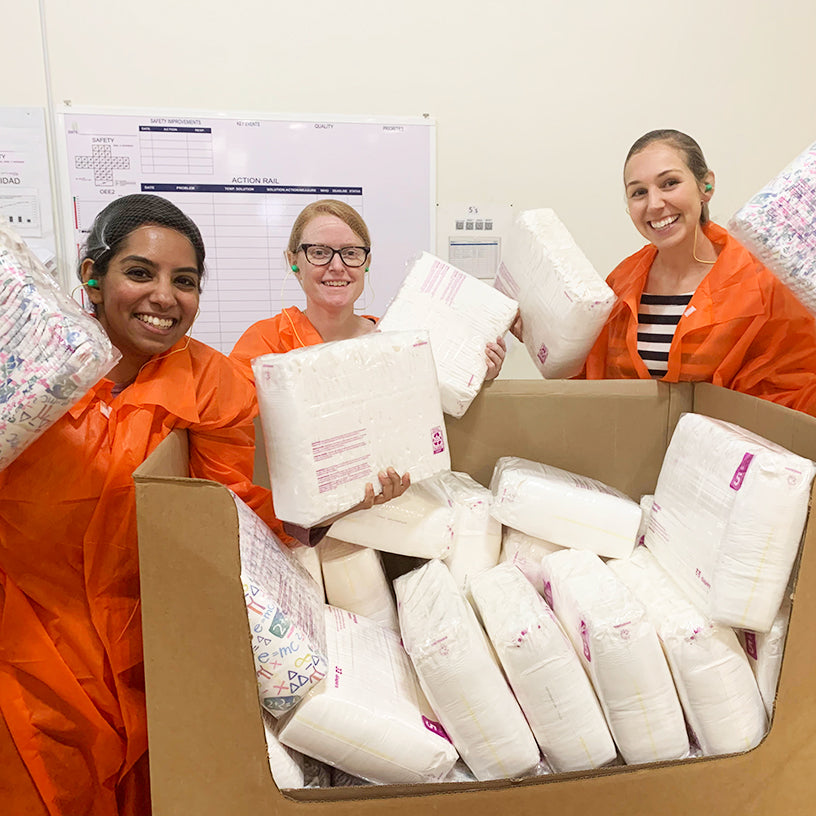 The Kudos Team: Amrita, Emily and Moira at a diaper factory holding diaper prototypes